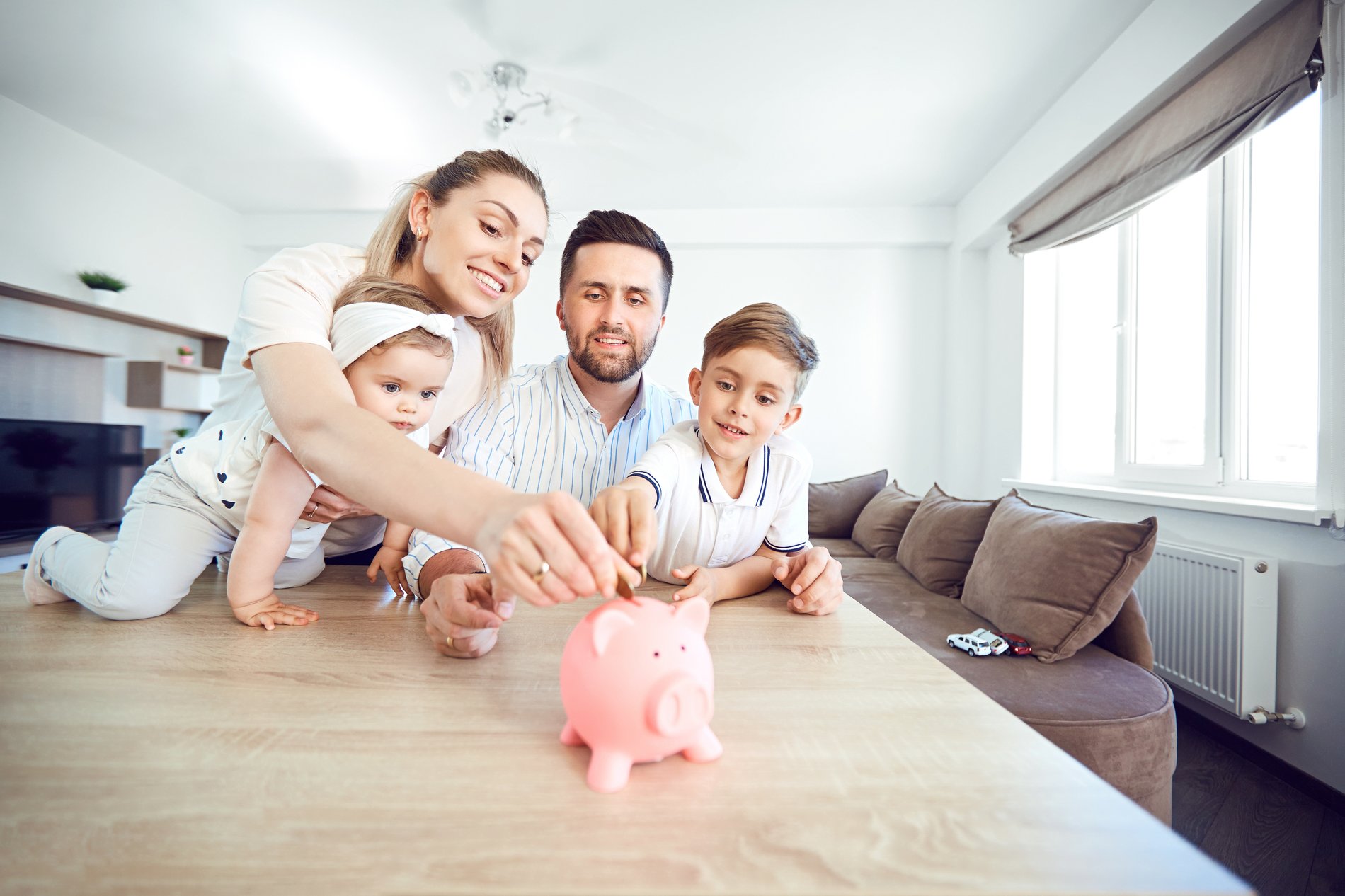 Eine glückliche Familie sitzt am Tisch und steckt Geld in eine Schweinspardose.