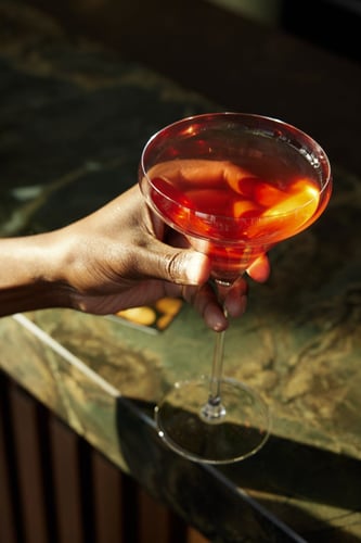 Woman holding a red alcoholic drink with an orange from the cloud one bar