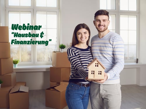 Paar steht vor Umzugskartons, hält Miniaturhaus in der Hand und lächelt in die Kamera - Webinar-Einladung "Hausbau & Finanzierung" - Versicherung Berlin-Adlershof