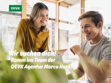 Mann sitzt, Frau steht, beide unterhalten sich lachend im Büro vor einem Laptop