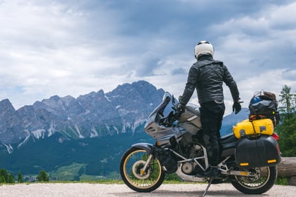 Auf dem Foto ist ein Motorradfahrer vor einer wunderschönen Bergwelt zu sehen. Auch auf Reisen mit dem Motorrad ist eine Auslandsreise-Krankenversicherung unverzichtbar.