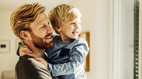 Bild von einem Vater mit seinem Sohn auf dem Arm. Beide schauen aus dem Fenster.