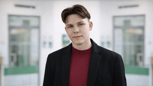 Foto zeigt Saimen Bethke lächelnd vor einer DEVK-Agentur Fassade