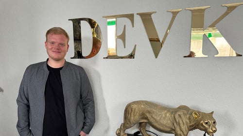 das Foto zeigt lächelnd den Versicherungsfachmann, Gian Luca Mai im schwarzen Outfit mit grauem Blazer