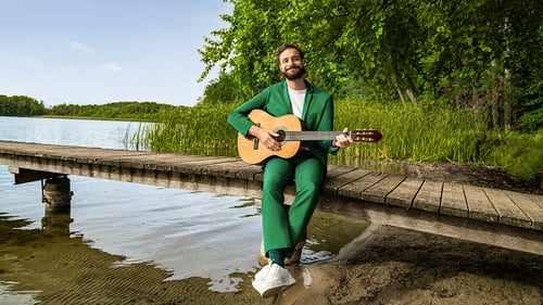 Mann sitzt mit Gitarre am See