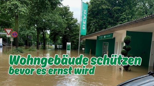 Hochwasser vor der DEVK Versicherungsagentur Cornelia Schreven-Herweg in Leverkusen. Die Straße und der Eingangsbereich sind überflutet, im Bild steht der Text „Wohngebäude schützen bevor es ernst wird“