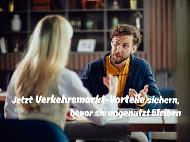 Blonde Frau und Mann mit orangem Pullover sitzen sich am Beratungstisch gegenüber - Beitrag zum Thema: Bahn, ÖPNV oder Logistik? Diese Versicherungsvorteile lassen viele liegen