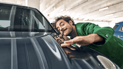 Motiv „Mann in einem grünen Anzug streicht mit Hand über
Motorhaube eines Autos.“