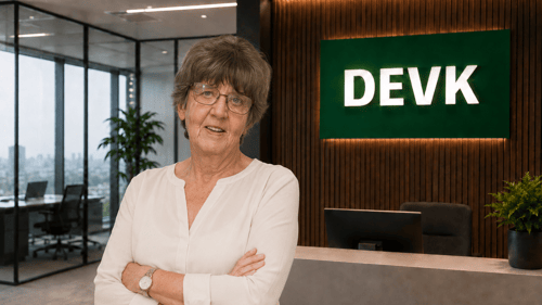 Das Foto zeigt eine Frau mit Brille und weißer Bluse in einem modernen Büro mit DEVK Logo
