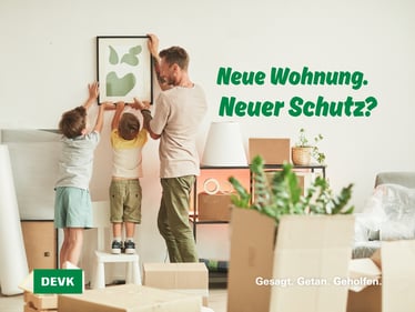 Vater und zwei Kinder richten gemeinsam ein Bild in der neuen Wohnung ein, umgeben von Umzugskartons und Möbeln. Bildtitel: Neue Wohnung. Neuer Schutz? Versicherungsschutz nach Umzug prüfen: Warum Hausrat und Wohngebäude in Augsburg jetzt wichtig sind