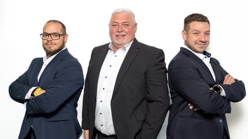 Drei Mitarbeiter der DEVK Versicherungsagentur Viktor Pfitzner in Würzburg stehen gemeinsam vor hellem Hintergrund. Das Team im Bürgerbräu präsentiert sich persönlich, freundlich und professionell.