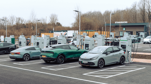 Multiple electric vehicles charging at InstaVolt ultra rapid chargers in a modern EV charging hub with a Starbucks café in the background.