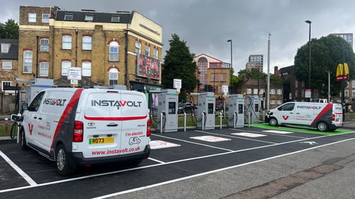 EV drivers charging at InstaVolt ultra-rapid chargers at Bestwood Retail Park in London, with McDonald's and local shops visible nearby.