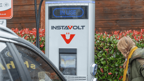 An InstaVolt ultra rapid EV charging station at McDonald’s Tonbridge in use, featuring a bright display and contactless payment option. A driver interacts with the charger in a clean, accessible environment surrounded by greenery.