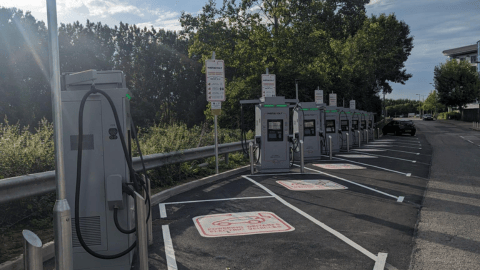 A row of InstaVolt ultra rapid electric vehicle chargers in a designated charging area, with a tree-lined background and clear markings on the ground.