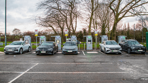 Electric vehicles charging at InstaVolt ultra-rapid chargers at Welcome Break Corley M6 Southbound, with trees and cloudy skies in the background.