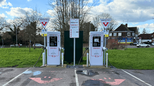 Two InstaVolt ultra rapid EV chargers in a car park with signage and a shopping precinct in the background.