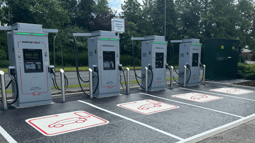 InstaVolt ultra-rapid EV chargers in a row at a dedicated charging bay, featuring four modern units with clear bay markings and surrounded by greenery.