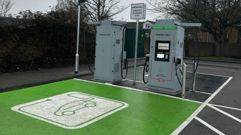 Two InstaVolt ultra rapid EV chargers on green parking bays with clear signage and a lamppost nearby, situated in a clean and spacious car park. Trees and fencing are visible in the background.