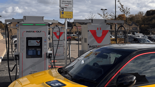 Multiple InstaVolt ultra-rapid EV chargers in use at a public car park, with a yellow and black electric vehicle parked in front and clear signage overhead.