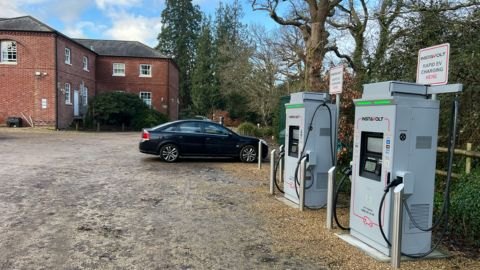 InstaVolt ultra rapid EV chargers in a gravel car park at Bartley Lodge Hotel, Cadnam, UK. A black car is parked nearby, with a red-brick hotel building and trees in the background. Signs indicate priority for rapid EV charging.