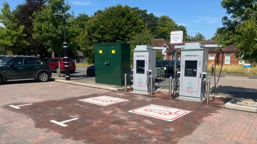 Ultra rapid InstaVolt charging bays in a shaded parking area, with a green utility box and nearby parked vehicles.