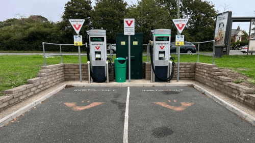An InstaVolt ultra rapid EV charger installed in an outdoor location, with a parking sign and road signs nearby. The charger is positioned on a concrete base with a railing around it.
