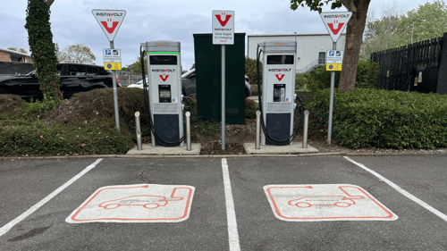 Two InstaVolt ultra rapid EV chargers with marked parking bays (86 and 87) in an outdoor charging station, surrounded by greenery and a van to the right.