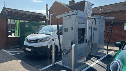InstaVolt ultra-rapid EV chargers installed in a car park next to a Co-operative store, with a white Toyota van and green electric vehicle plugged in.