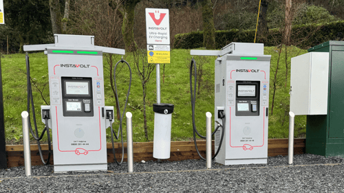 Two InstaVolt ultra-rapid EV chargers installed at Plas Weunydd Hotel with contactless payment screens and charging cables, set against a wooded hillside.