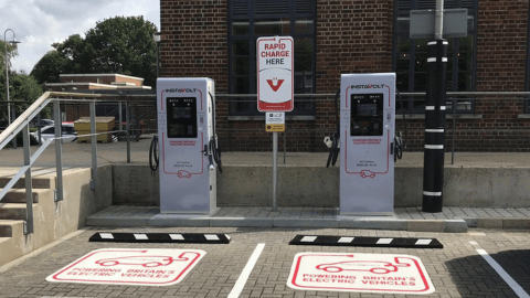 Two InstaVolt ultra rapid EV chargers in a designated parking area with clear markings and a 'Rapid Charge Here' sign, set against a brick building backdrop