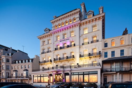 Exterior shot of Mercure Brighton Seafront Hotel with pink spotlights on hotel front, dusk, sunset reflection in windows