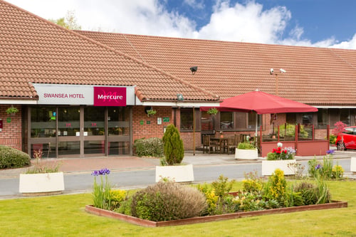 Exterior shot of Mercure Swansea Hotel, flower bed, patio area, front door
